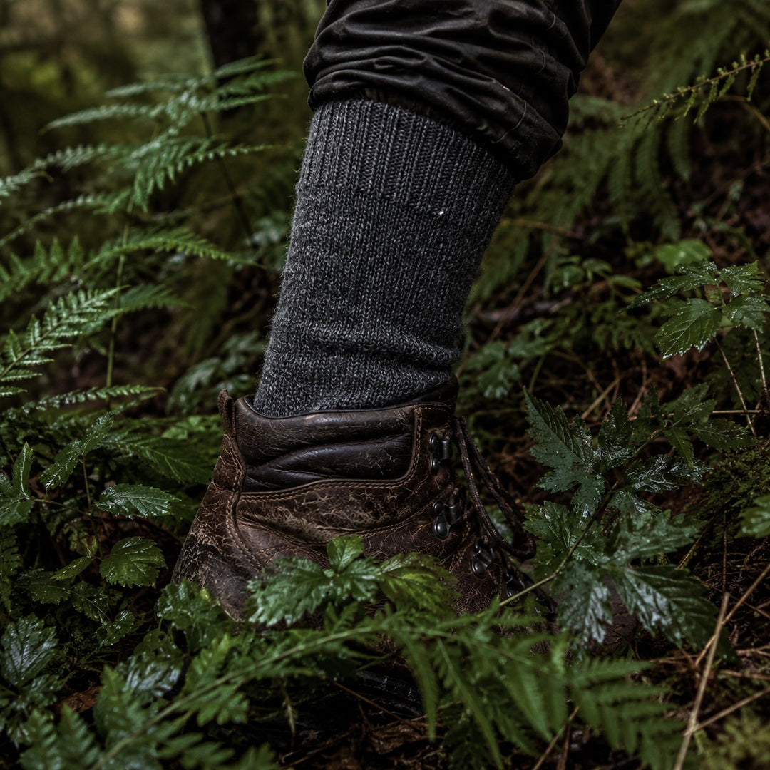 Dark gray knitted wool sock over a hiking boot in dense green undergrowth